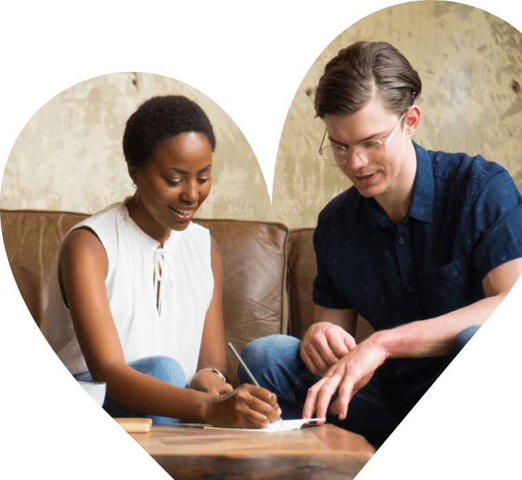 A heart shaped image of 2 people signing something on a low table they both look happy